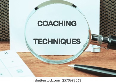 Personal development and self improvement. The concept of technology and business development. The concept phrase COACHING TECHNIQUES on a white sheet through a magnifying glass, front view.