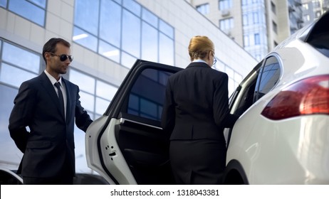 Personal Driver Waiting For Boss On Parking Lot, Helping Her To Get Into Car