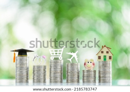 Personal expense and weekly budget, financial concept : Six coin stacks with logos on top e.g a black graduation cap, a wedding or engagement rings, a shopping cart, a house, a plane, a piggy bank.