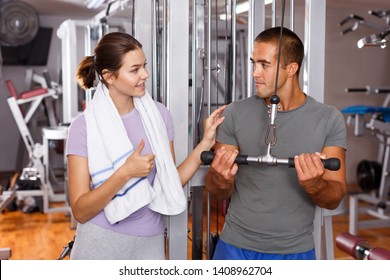 Personal Instructor Helping Young Woman With Exercise Technique At Gym