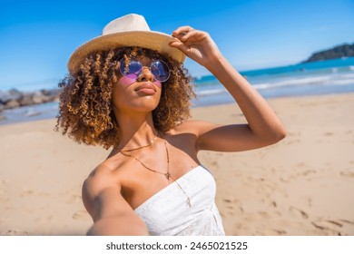 Personal perspective of a beauty latin young woman wearing sunglasses and sun hat taking a selfie enjoying summer at sandy beach - Powered by Shutterstock