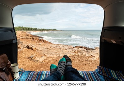 Personal perspective of feet in warm socks inside a camper van with the door open and views at a mediterranean coast. - Powered by Shutterstock