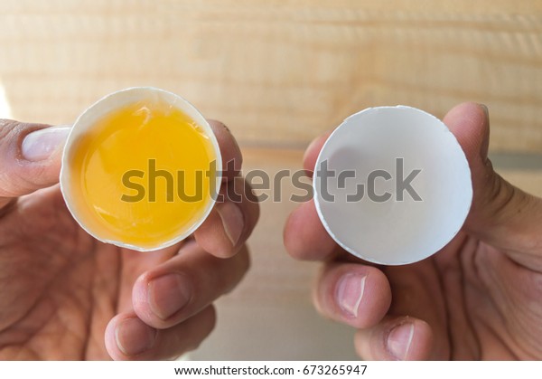 Personal perspective of a person with an egg\
divided in two parts in his\
hands