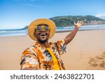 Personal point of view of a young african man in colorful clothes, sunglasses and hat taking a selfie enjoying holidays on the beach