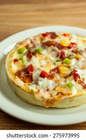 A Personal Sized Deep Dish Pizza On A White Plate, Sitting On A Wooden Table.