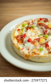 A Personal Sized Deep Dish Pizza On A White Plate, Sitting On A Wooden Table.