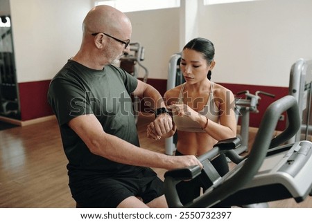Personal Trainer Adjusting Smartwatch for Client in Gym