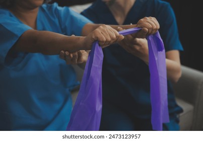 Personal trainer assisting senior woman with resistance band. Rehabilitation physiotherapy worker helping old patient at nursing home. Old woman with stretch band being coached by physiotherapist. - Powered by Shutterstock