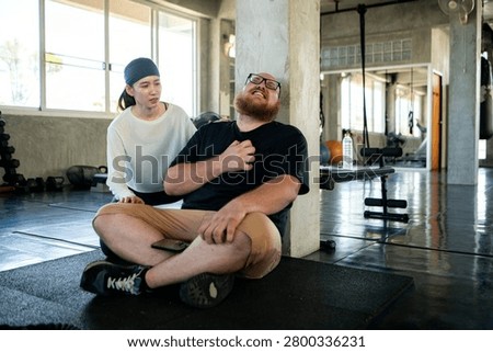 Personal trainer checking on an exhausted beginner who experienced shortness of breath and chest pain from fatigue after strenuous exercise