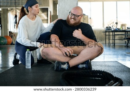 Personal trainer checking on an exhausted beginner who experienced shortness of breath and chest pain from fatigue after strenuous exercise