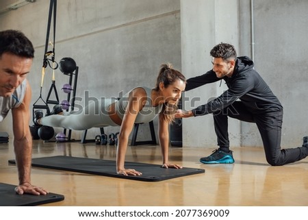Personal trainer corrects woman's plank position at gym.
