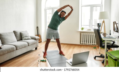 Personal Trainer. Full Length Shot Of Male Fitness Instructor Stretching His Body While Streaming, Broadcasting Video Lesson On Training At Home Using Laptop. Sport, Online Gym Concept. Web Banner