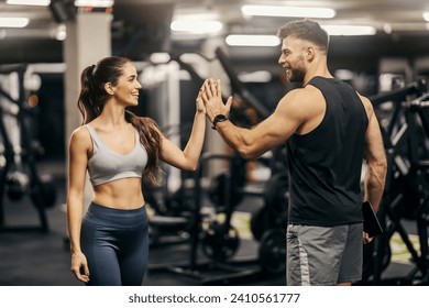 A personal trainer is giving high five to a fit sportswoman in a gym. - Powered by Shutterstock