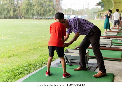 Personal Trainer Giving Lesson To Young Boy In Golf Driving Range.