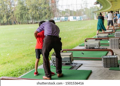 Personal Trainer Giving Lesson To Young Boy In Golf Driving Range.