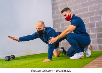 Personal trainer in the gym correcting the stretching of the student on the floor in the coronavirus pandemic, a new normal. With protective face mask