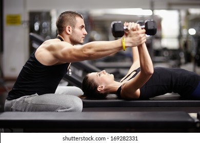 Personal trainer helping woman working with heavy dumbbells