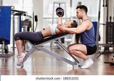 Personal trainer helping woman working with dumbbells