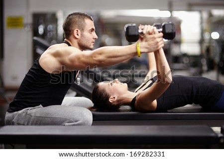 Personal trainer helping woman working with heavy dumbbells