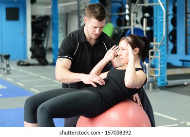 Personal Trainer Helping Young Woman In Gym