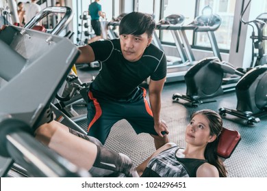 Personal Trainer Helps His Female Client Working At Leg Press In The Gym. Concept Of Indoor Fitness Healthy Lifestyle.