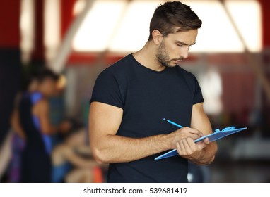 Personal Trainer Holding Clipboard And Writing Training Plan In Gym