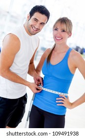 Personal trainer measuring a woman waist at the gym