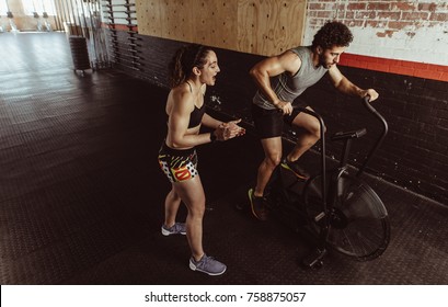 Personal trainer motivating man exercising on air bike in gym. Man doing intense workout on gym bike with female coach. - Powered by Shutterstock