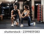 Personal trainer is showing a sportswoman how to do lunges correctly while kneeling in a gym.