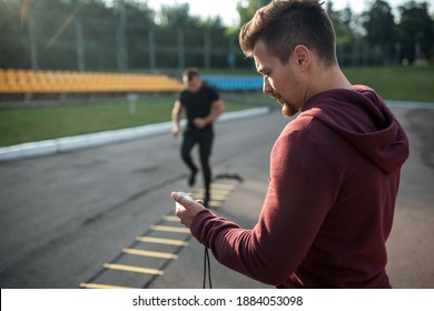 personal trainer with stopwatch measuring time of male exercising outdoor - Powered by Shutterstock