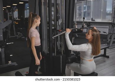 Personal Trainer Teaching Teen Girl Working Out On Lat Pull Down Gym Machine