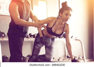 Personal Training Men Help Women's Arms To Pull Up Dumbbell For Exercise At Indoor Gym.