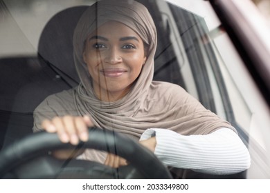 Personal transport, driver on city street, driving lesson, enjoying trip or road to office. Happy young cute african american muslim woman in hijab driving car on steering wheel, free space, close up - Powered by Shutterstock