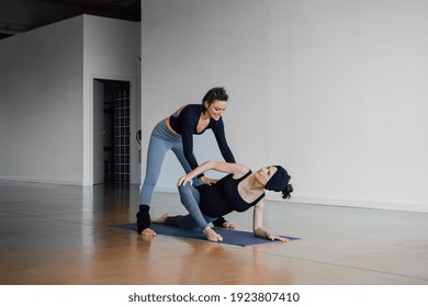 Personal yoga instructor teaching to her pregnant student yoga on mat in studio, practicing Parivrtta Anjaneyasana crescent lunge on knee, in a modern gym. Prenatal classes - Powered by Shutterstock