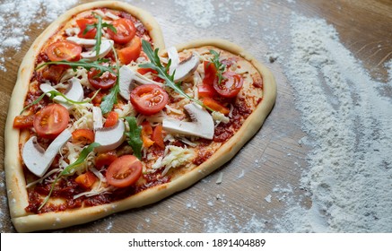 Personalized order of heart-shaped pizza for a holiday to celebrate at home. Place on the floured table in the left corner. The pizzeria is open on the eve of Valentine's Day. - Powered by Shutterstock