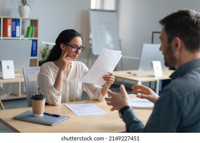 Personnel manager communicating with vacancy candidate, reading resume during job interview at office. Focused female HR specialist studying applicant's CV. Headhunting and personnel rectuitment