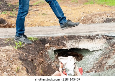 Person's Feet Step Over A Hole Near An Asphalt Sidewalk.