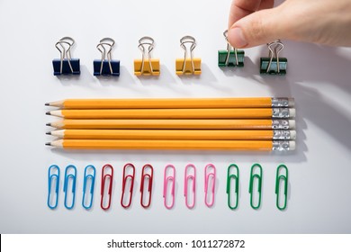 Person's Finger Arranging The Pencils With Row Of Pins Rubber And Pen On White Background