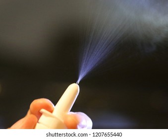 Person's Fingers Pressing On A White Nasal Spray Pump With Mist Being Sprayed From The Nozzle