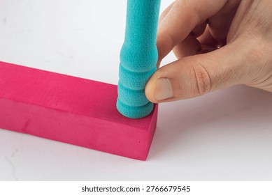 a person's hand carefully assembling a turquoise foam peg into a bright pink base. This image highlights manual dexterity, toy assembly, and the soft texture of EVA foam materials
