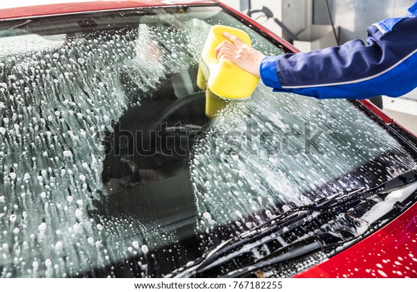 Person\'s Hand Cleaning Car Windshield With Sponge\
At Service Station