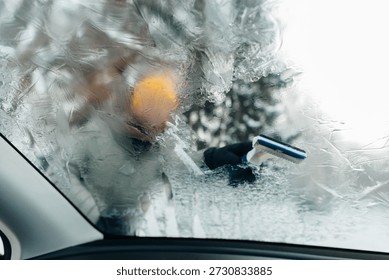 Person's hand clearing ice with an ice scraper from a frosted car windscreen on a cold winter morning