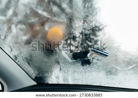 Person's hand clearing ice with an ice scraper from a frosted car windscreen on a cold winter morning