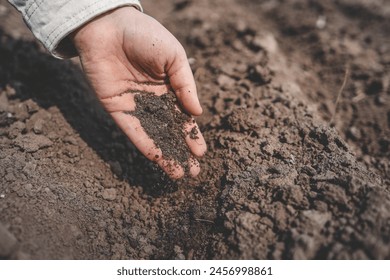 The persons hand clenches a handful of dirt, feeling the texture with their fingers. Their thumb digs into the soil as they stand on grass and asphalt next to an automotive tire - Powered by Shutterstock