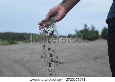A person's hand dropping grains of sand in an open field. Symbolizing passing time or letting go