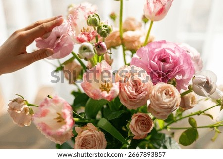 Person's hand gently touching delicate pink ranunculus bouquet showcasing tender care and appreciation for beautiful spring flowers