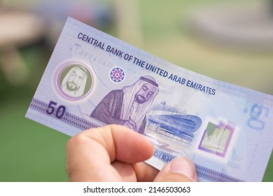 Persons hand giving the Currency of the United Arab Emirates (UAE) - New 2021 Fifty Dirham notes spread out on a green background. Money exchange. - Shutterstock ID 2146503063