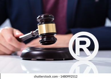 A Person's Hand Hitting The Gavel On Sounding Block Near Trademark Icon Over Desk