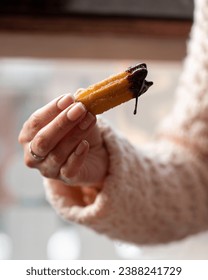 A person's hand holding a freshly dipped churro with dripping chocolate sauce, embodying a moment of sweet indulgence