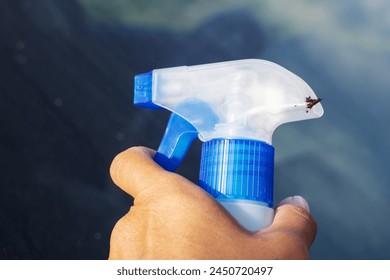 The persons hand is holding a plastic bottle filled with electric blue liquid. A bug is perched on the bottle as the finger hovers over the spray nozzle - Powered by Shutterstock